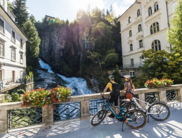 Cyklisté pozorují z mostu mohutný vodopád v centru města Bad Gastein