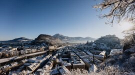 Zasněžená městská krajina s horami, jasnou modrou oblohou a pohledem na Hohensalzburg