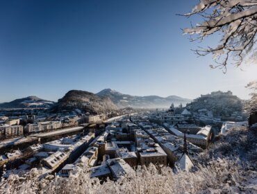 Zasněžená městská krajina s horami, jasnou modrou oblohou a pohledem na Hohensalzburg
