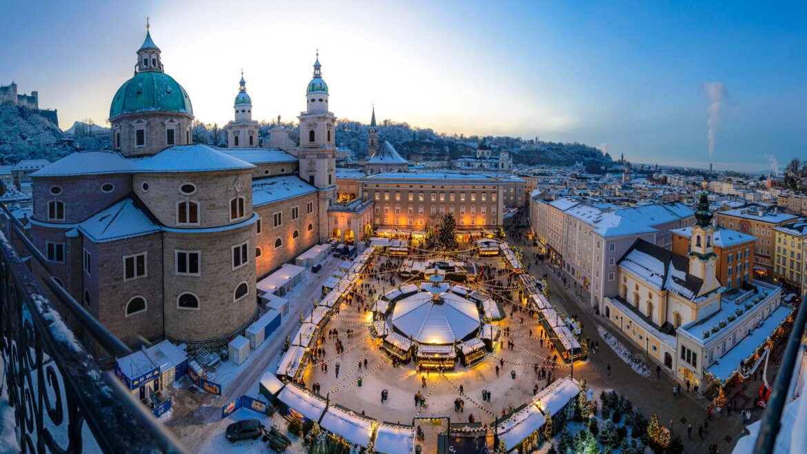 Pohled na adventní trh v centru Salcburku, Ježíškův Christkindlmarkt s osvětlenými stánky a katedrálou z výšky