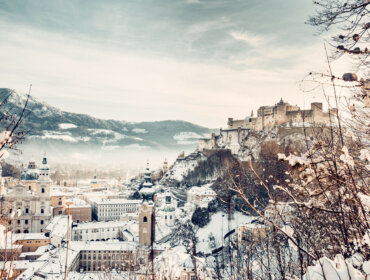 Salcburk se zasněženými střechami kostelů a domů s dominantou, pevností Hohensalzburg