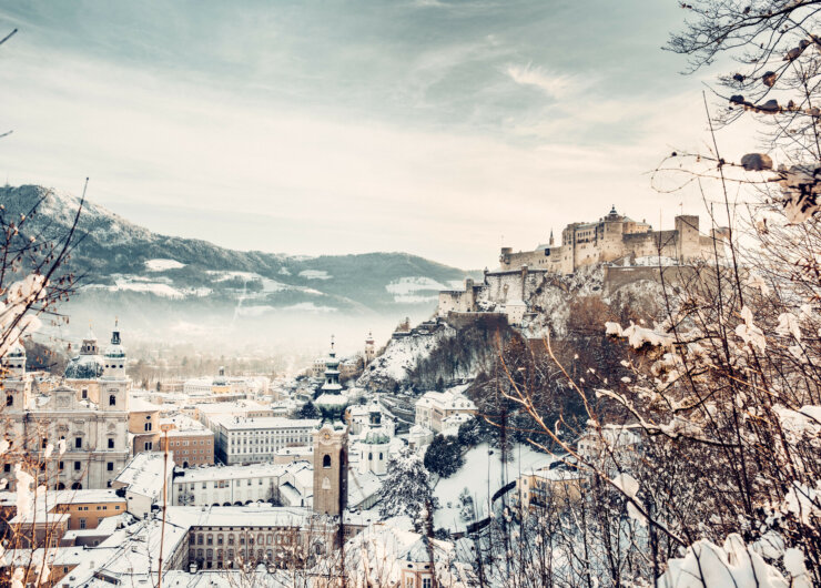 Salcburk se zasněženými střechami kostelů a domů s dominantou, pevností Hohensalzburg