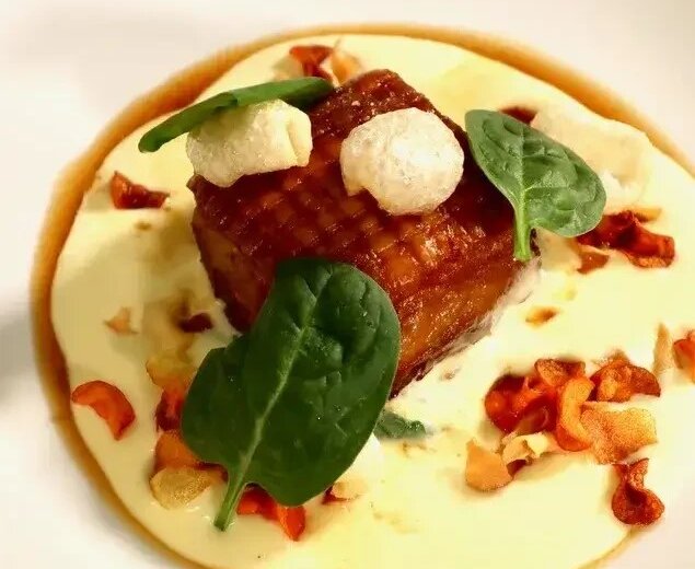 Knuspriger Schweinebauch, Erdäpfelschaum,Bärlauchspinat_GT42_©SAM-Elisabeth Eisl A gourmet recept bůček s bramborovou pěnou a špenátem, servírovaný s křupavými toppingy na bílém talíři.