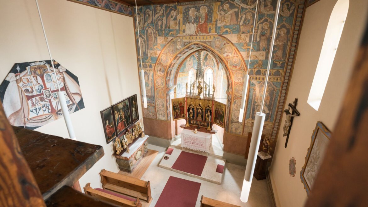 Pohled shora na interiér kaple na hradě Mauterndorfu s freskami, lavicemi a oltářem.