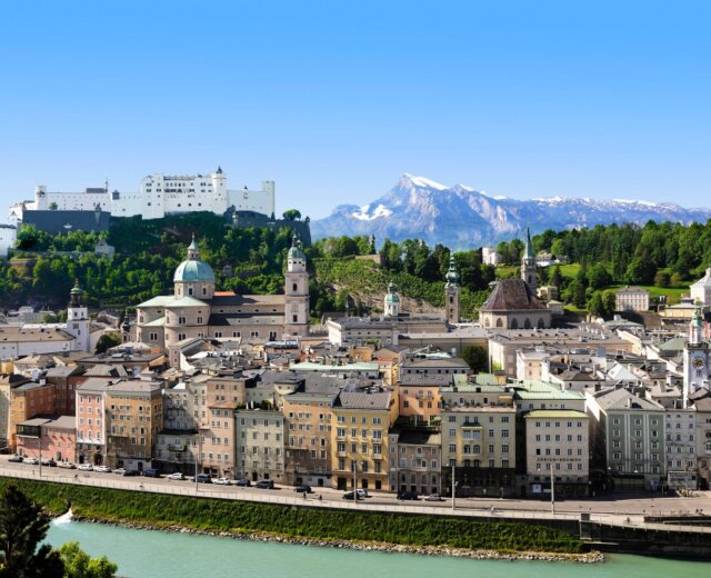 Pevnost Hohensalzburg z dálky, zasazená do městské a horské krajiny.