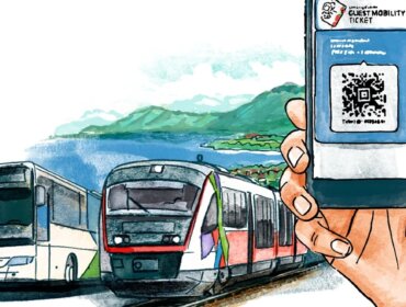 Ruka držící telefon s jízdenkou pro hosty, v blízkosti autobusu a vlaku u malebného jezera a hor.