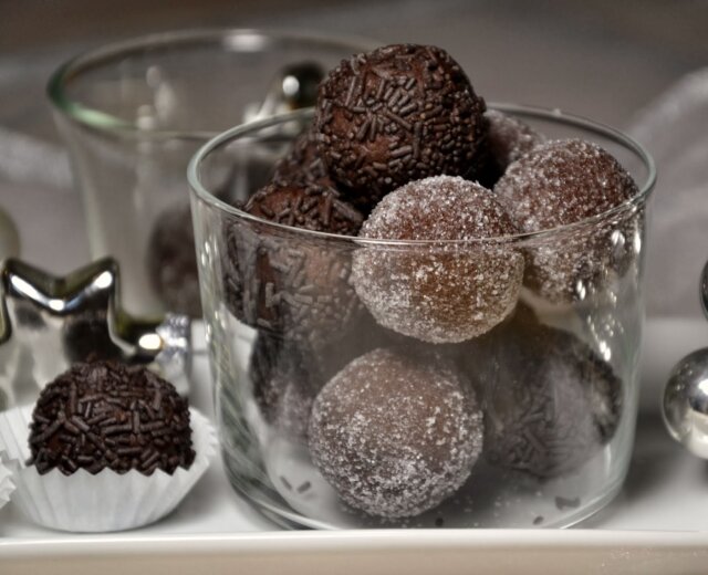 Čokoládové kuličky obalené cukrem a posypané ve skleněné míse, se slavnostními dekoracemi poblíž.