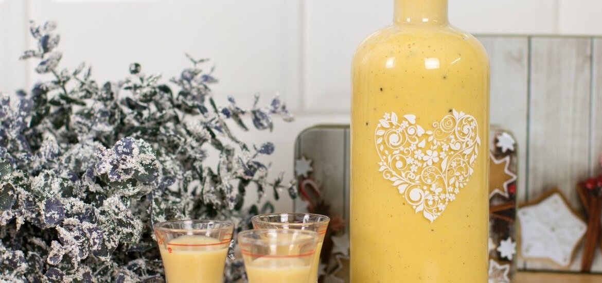 Láhev a sklenice žlutého vaječného koňaku z Domácího vaječného likéru, se sušenkami a zasněženou zelení.