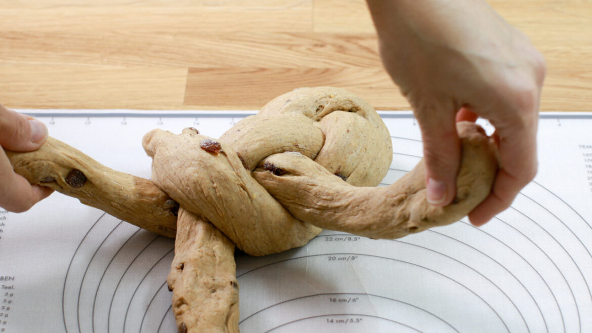 © Anke Eder Ruce pletoucí těsto s rozinkami na podložce na pečení s vyznačenými mírami. (Zvětšený pohled)