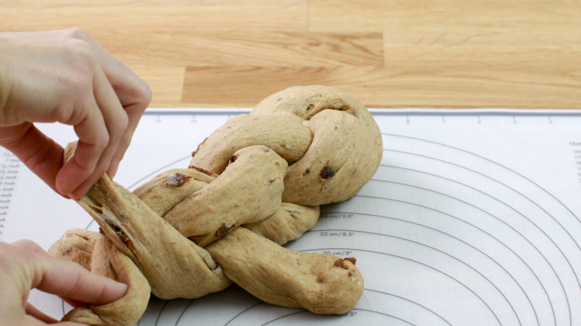 © Anke Eder Ruce pletoucí těsto s ořechy na bílé podložce na pečení s vodítky na dřevěném pultu. (Zvětšený pohled)