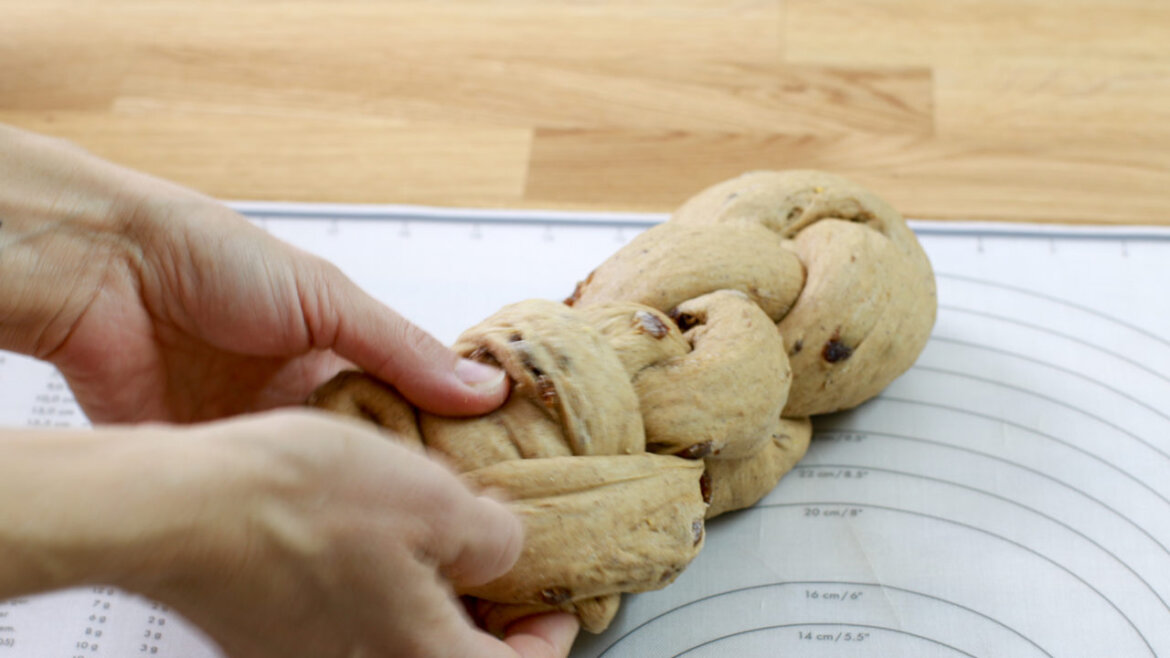 © Anke Eder Ruce pletoucí těsto s rozinkami na podložce na pečení s vodítky na dřevěném povrchu. (Zvětšený pohled)