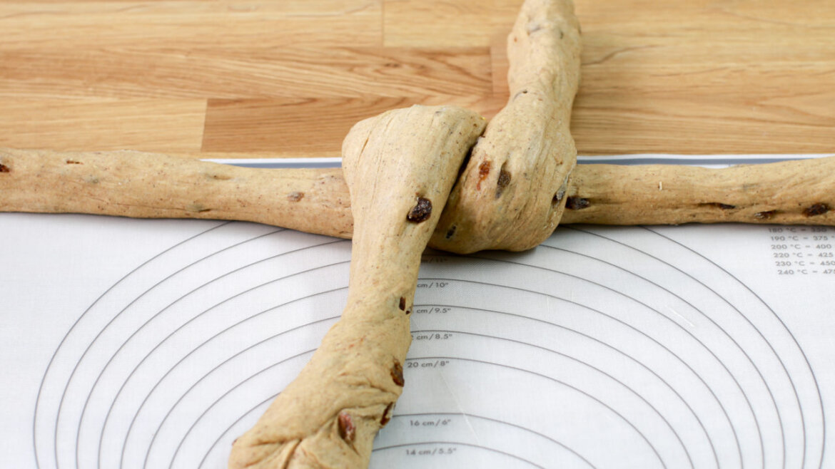 © Anke Eder Dva kusy chlebového těsta, jeden stočený přes druhý, na kruhové podložce a dřevěném povrchu. (Zvětšený pohled)