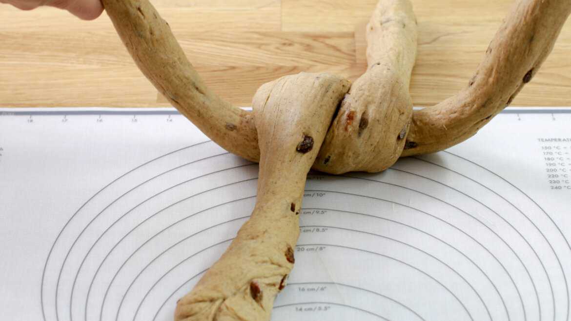 © Anke Eder Ruce pletoucí těsto s rozinkami na podložce s kruhovými rozměry, v pozadí dřevěný povrch. (Zvětšený pohled)