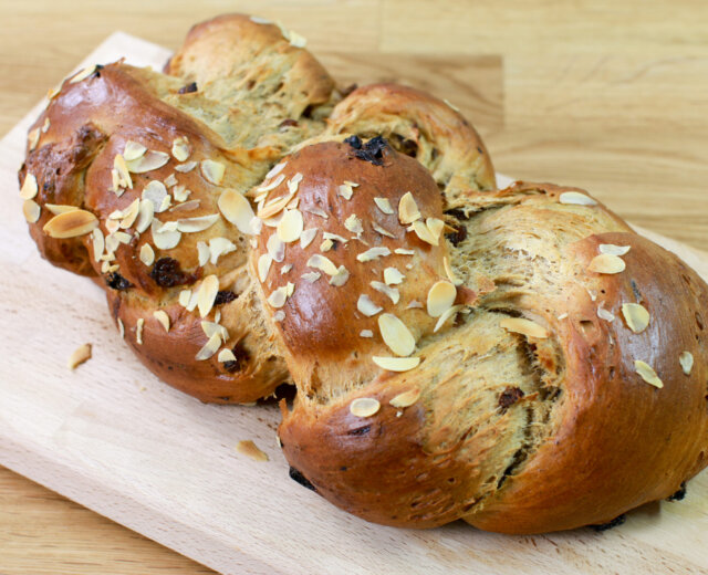 Vánočka s rozinkami a plátky mandlí položená na dřevěném prkénku.