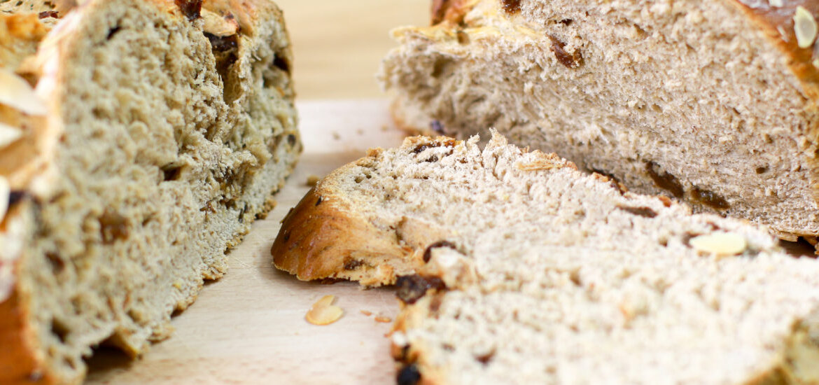 Detailní záběr na rozkrojenou Vánočku s rozinkami na dřevěném prkénku.