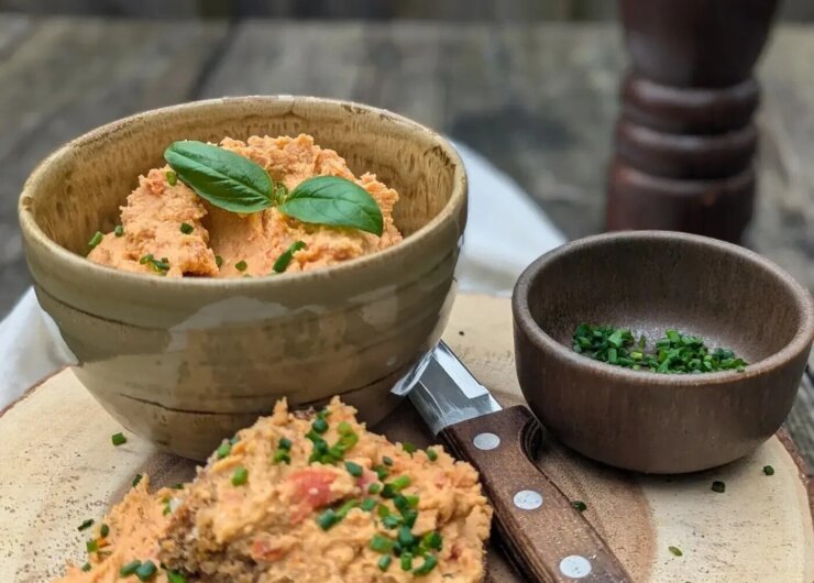 Miska čočkové pomazánky s bazalkou, plátky chleba potřené pomazánkou, pažitka a nůž na dřevěném prkénku.