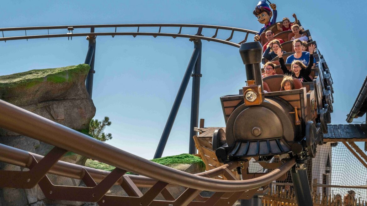 Lidé jedoucí na venkovní horské dráze s vlakovou tematikou v Salcburské zemi jezer, usmívající se vzrušením.