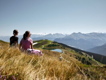 Dva lidé sedí ve vysoké trávě s výhledem na Mittersill v létě a národní park Vysoké Taury.