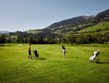 Dva lidé hrající golf na zeleném hřišti v Mittersillu v létě, v pozadí hory.