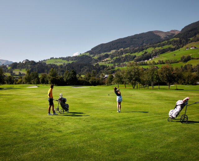 Dva lidé hrající golf na zeleném hřišti v Mittersillu v létě, v pozadí hory.
