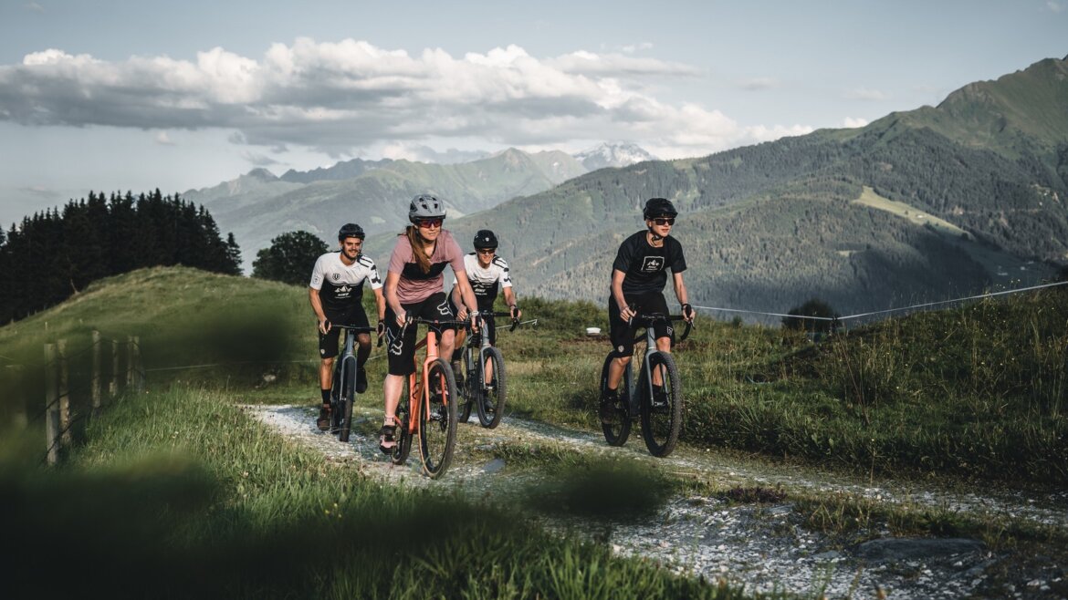 Čtyři cyklisté jedou na horských kolech po šotolinové stezce v národním parku Vysoké Taury u Mittersillu v létě.
