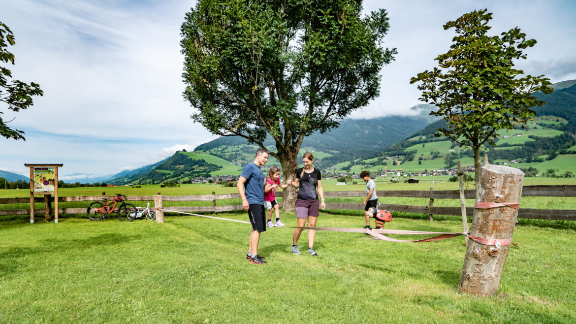 Rodina odpočívá na lavičce u cyklostezky Tauernradweg s výhledem na řeku Salzach a okolní hory (Zvětšený pohled)
