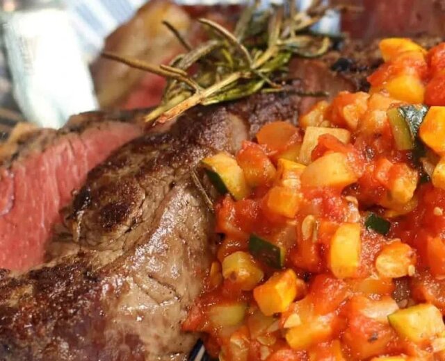 Steak propečený na „medium-rare“ s přílohou nakrájené zeleniny v rajčatové omáčce, podávaný na talíři s modrobílým vzorem.