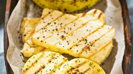Gegrillter Käse mit Kräutermarinade © Canva.png Grilované plátky sýra halloumi a kolečka bylinkového sýra na plechu vyloženém pergamenovým papírem.