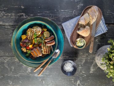 Grillgemüse, Grillkäse und Grillwürstl©Salzburger Agrar Marketing-Martina Höfelmaier Grilované klobásy a zelenina v misce, chléb a máslo na prkénku, sůl v malé misce.