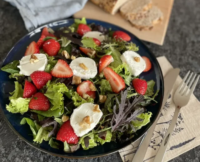 Salat m Erdbeeren©SAM-Marion Riepler.JPEG Letní salát s jahodami, kozím sýrem, vlašskými ořechy a míchaným salátem, v pozadí je nakrájený chléb.