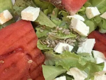 Salat-mit-gegrillter-Wassermelone_Ulli Hammerl Salát, plátky grilovaného vodního melounu, kostkami sýra a slunečnicovými semínky na bílém talíři.