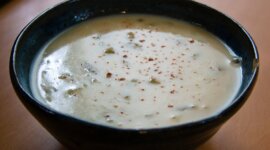 cremige Kartoffelsuppe in einer Schale Na dřevěné desce stojí tmavá miska krémově bílé bramborové polévky, posypaná kořením.