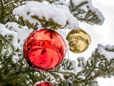 Nærbillede af rød og guld pynt, der hænger på et snedækket juletræ på et festligt julemarked.