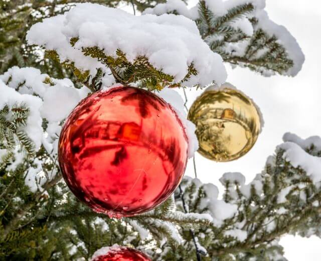 Nærbillede af rød og guld pynt, der hænger på et snedækket juletræ på et festligt julemarked.