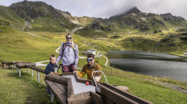 Familien spiller udendørs træspil ved en bjergsø og drømmer om at stå på ski i Obertauerns naturskønne bjerge.