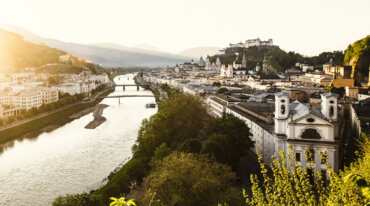 En naturskøn udsigt over Salzburg, Østrig, med en flod, broer, historiske bygninger og skiløjper ved solnedgang.