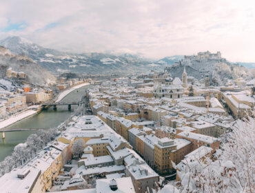 verschneite Stadt Salzburg Snedækkede hustage i en europæisk by under en regnvejrshimmel med broer og bjerge bagved.