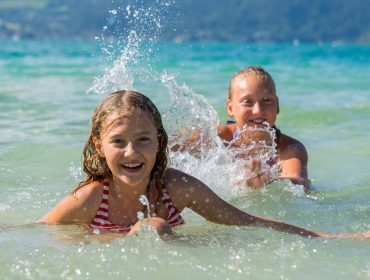 To smilende børn leger og plasker i klart blåt vand på en solskinsdag med gratis adgang.