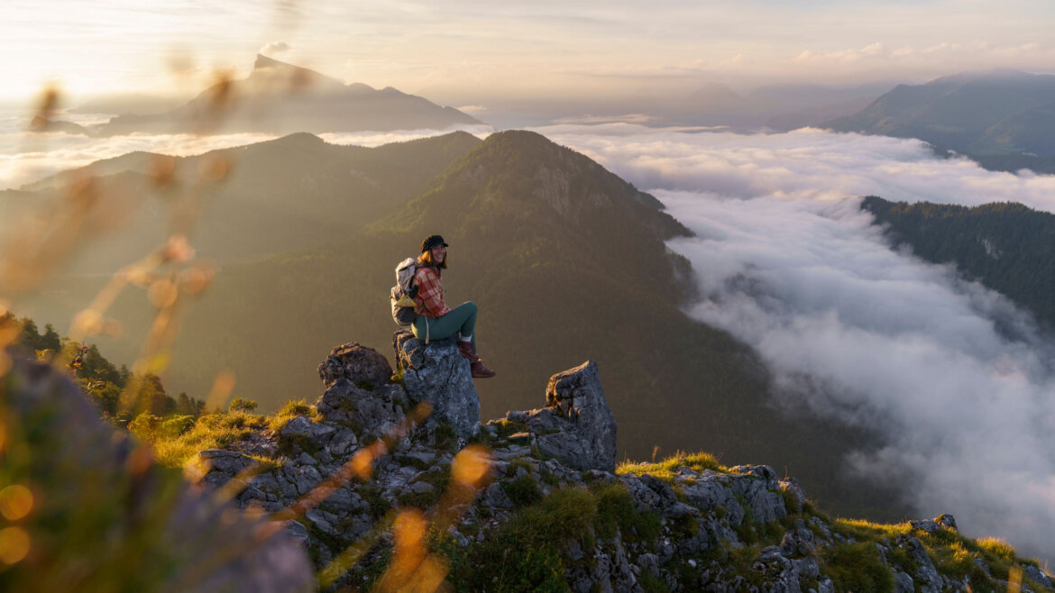 En vandrer sidder på en klippefyldt bjergtop og kigger ud over tågede dale og skidækkede bakker ved solopgang. (Forstørret visning)