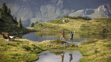 To mennesker vandrer ved en bjergsø; grønne bakker antyder Obertauerns skiløjper i det fjerne.