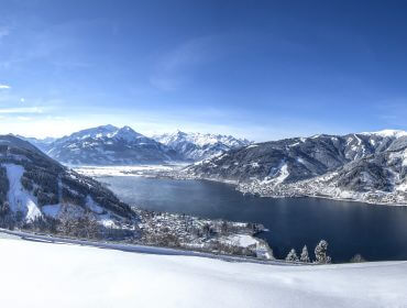 Snedækkede bjerge og en sø skinner under den skarpe sol i Zell am See-Kapruns vinterlandskab.