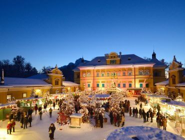 Et festligt Julemarked fylder et snedækket torv i skumringen med mennesker og farverige lys.