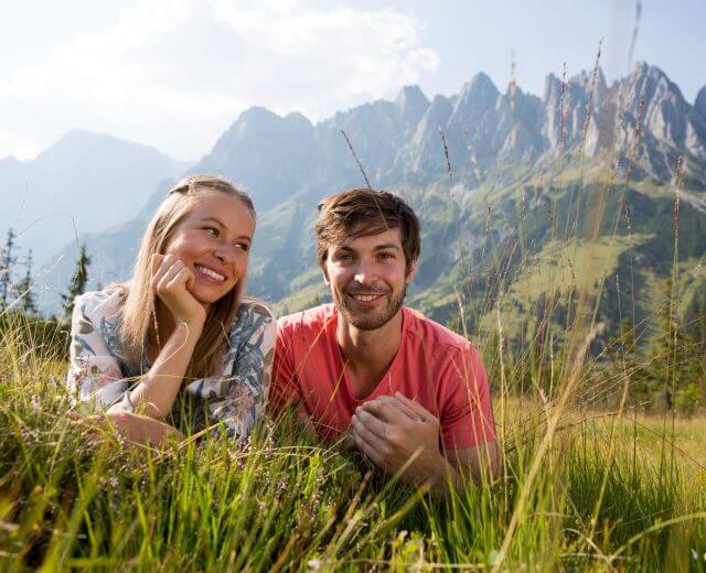 huttenurlaub-entschleunigung Et smilende par ligger på græsset foran bjerge på en solskinsdag.