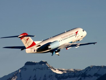 Austrian Airlines-flyet letter med sneklædte bjerge i baggrunden under en klar himmel.