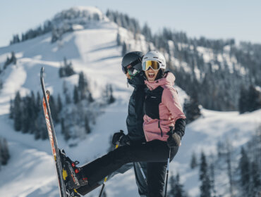 P1150338 To skiløbere poserer legende på et snedækket St. Johann i Salzburg-bjerg, mens de smiler iført skitøj og skibriller.