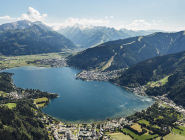 En stor sø omgivet af grønne bjerge og spredte byer under en klar blå himmel.
