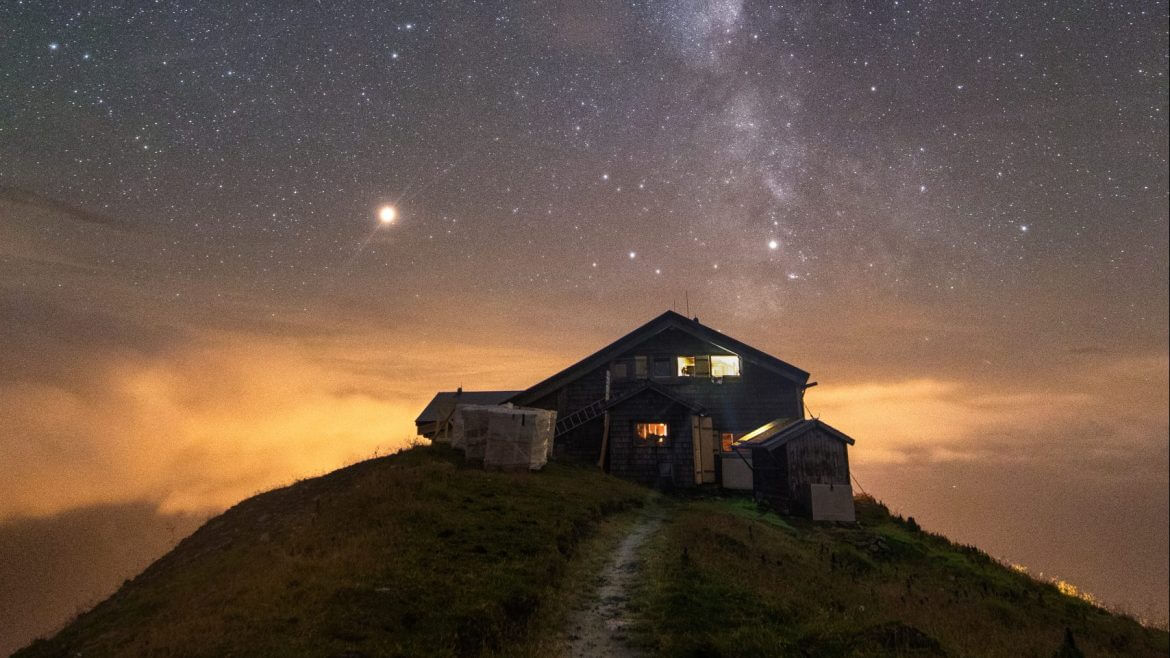 © BRANISLAV ROHAL En hytte på en bakketop om natten, under en stjerneklar himmel med Mælkevejen og lysende skyer nedenunder. (Forstørret visning)