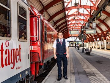 En togkonduktør står på en perron ved siden af et rødt tog på SalzburgerLands overdækkede banegård.