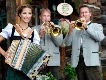 Drei Personen in traditioneller österreichischer Kleidung spielen Akkordeon und Trompeten bei einem rustikalen Bauernherbstfest.
