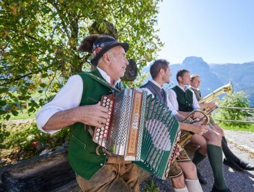 Bauernherbst Vier Männer in traditioneller österreichischer Kleidung musizieren beim Bauernherbst im Freien mit den Bergen im Hintergrund.